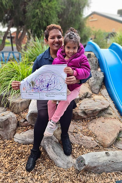 Jasmine, 4, sits with her mum Sam and shows her 'Important to Me' artwork